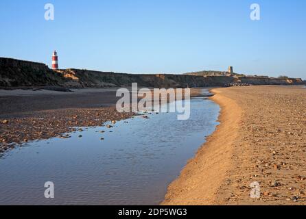 A view along the beach at low water in winter with pool and sandbank and the lighthouse above the cliffs at Happisburgh, Norfolk, England, UK. Stock Photo