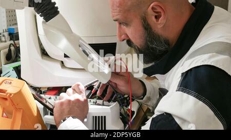 Electronics Maintenance Engineer Soldering Motherboard, Microchip and Circuit Board, Looking through Magnifying Glass. Electronics Repair and Testing Stock Photo