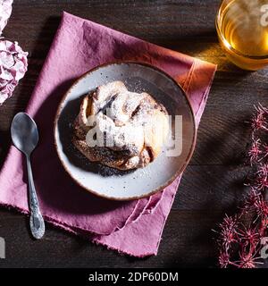 Tea Time - steaming tea with a nut cookie sprinkled with powdered sugar on a brown wooden table decorated with flowers Stock Photo