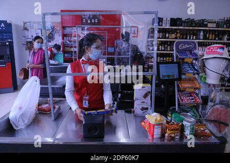 Supermarket cashier at a checkout counter wears a protective face mask & face shield behind a homemade plastic shield during the coronavirus pandemic. Phnom Penh, Cambodia. © Kraig Lieb Stock Photo