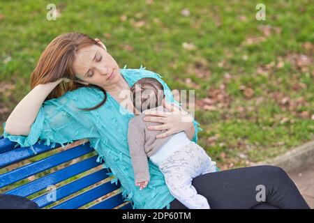 beautiful woman resting on a park bench with her baby on top. Lifestyle. maternity toughness concept Stock Photo