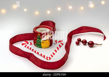 Christmas composition with Santa Claus burning candle, candy canes, red berries and ribbon and fairy lights, over white background Stock Photo