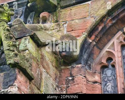 An old face and head carved in sandstone on the exterior of St Oswald's Parish Church in Malpas, Cheshire, UK. Stock Photo