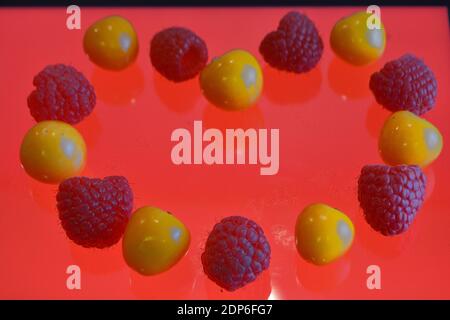 Pattern of kumquats and raspberries on an orange glassy background Stock Photo