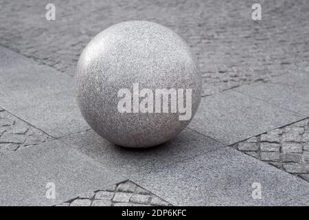 gray granite ball on the pedestrian sidewalk on a paving square with stone tiles, cityscape urban street architecture element, nobody. Stock Photo