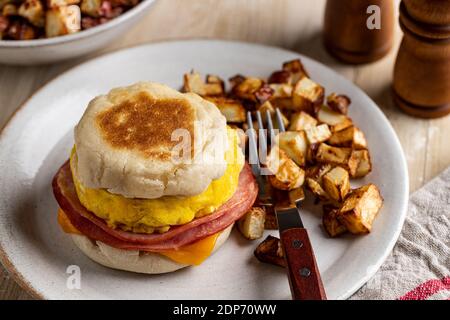 Breakfast sandwich with egg, ham and cheese on an english muffin with fried potatoes on a plate Stock Photo