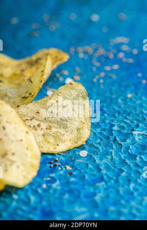 Homemade crispy potato chips with italian spices on the blue rustic background. Selective focus. Stock Photo