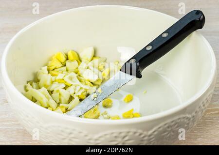 Chicken egg hard boiled sliced in white salad bowl on wooden table background, knife Stock Photo