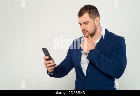Athletically built young business man in a suit and black shirt reading something in mobile phone on a white background isolated Stock Photo