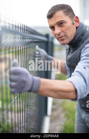worker installing welded metal mesh fence Stock Photo
