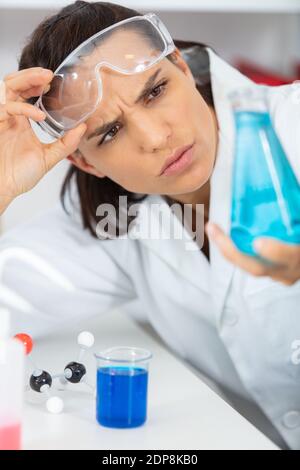 scientist dropping a blue solution into science bottle and looking Stock Photo