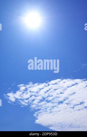 Vertical Image of the Bright Sun Shining above Altocumulus Clouds on Vibrant Blue Sky Stock Photo