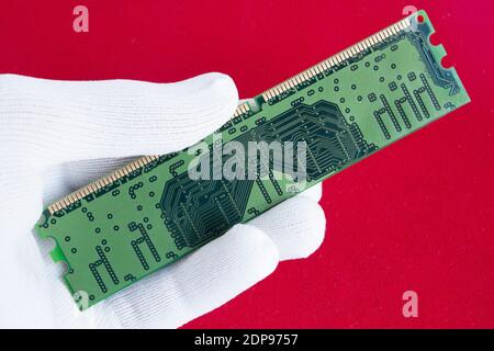 Hand in white glove holds a computer microchip. Isolated on a red background. Close up. Stock Photo