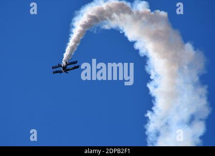 Pitts Model 12  stunt biplane performing   with smoke trail and blue sky. Stock Photo
