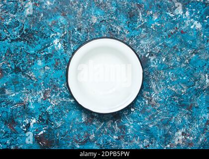 White enamel bowl on a blue concrete background. Top view Stock Photo
