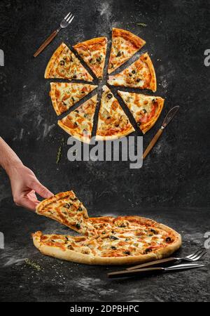 Home made original italian pizza with human hand holding pizza slice. Top view separated pizza slices on black grunge background Stock Photo