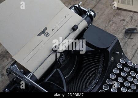 Wartime German field typewriter on desk with letter document bearing eagle and swastika at war and peace reenactment show. Stock Photo