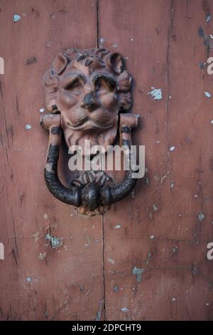 weathered and rusty head lion knocker old style on a door of abandoned house in  Sicily, evidences of culture and tradition Stock Photo