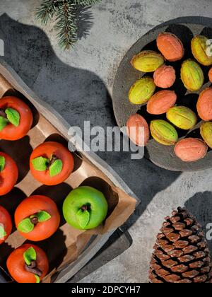 Marzipan sponge apples and sweetened condensed milk-filled walnuts. Tasty creative dessert assortment in green and red on rustic wood. Flat lay, long Stock Photo