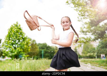 Happy smiling little girl throws up her backpack, outdoors in school playground Stock Photo