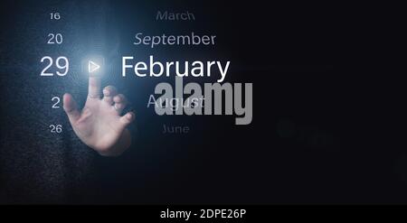 February 29th. Day 29 of month, Calendar date. Hand click luminous icon PLAY and DATE on dark blue background. Winter month, day of the year concept Stock Photo