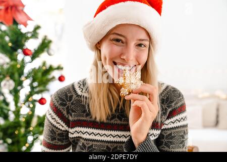 Close up of a happy pretty woman in santa hat eating bisquits with a christmas tree on a background Stock Photo