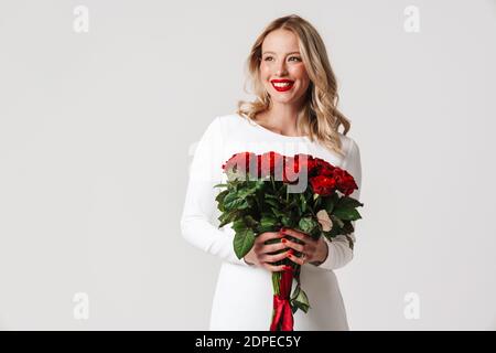Photo of a young happy dreaming woman in white dress holding red roses isolated over white background Stock Photo