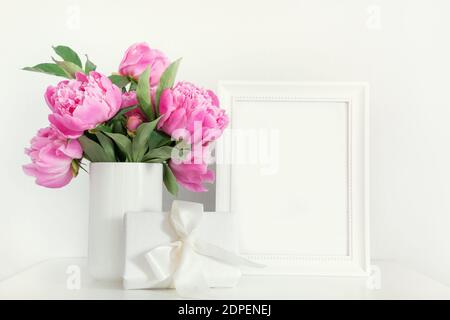 Pink peony in vase with gift photo frame on white. Mothers day. Cozy white interior. Stock Photo
