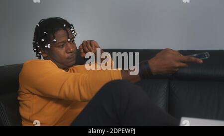 Relaxed young black man watching tv at home, changing the channels using remote controller. High quality photo Stock Photo