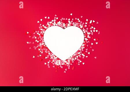 White heart and colored confetti on a red background. Stock Photo