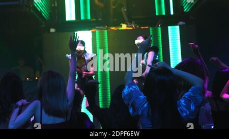 Group of people dance in disco night club to the beat of music from DJ on stage . New year night party and nightlife concept . Stock Photo