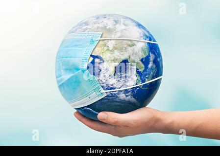 Hand holding Earth globe with face mask. World pandemic concept. Elements of this image furnished by NASA Stock Photo