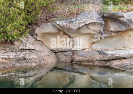 Warm colour tones and curving lines of smooth sandstone with overhanging arches are reflected in the calm water below, forming a semi-abstract scene. Stock Photo