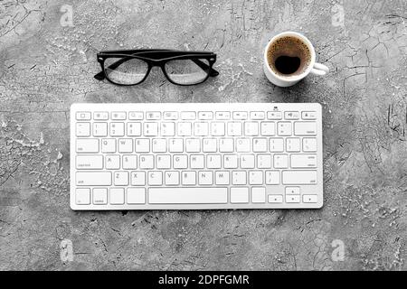 Computer keyboard, cup of coffee and eyeglasses on gray background Stock Photo
