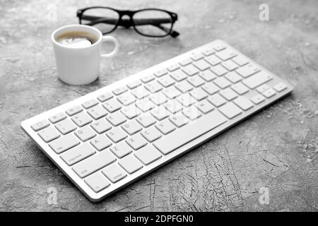 Computer keyboard, cup of coffee and eyeglasses on gray background Stock Photo