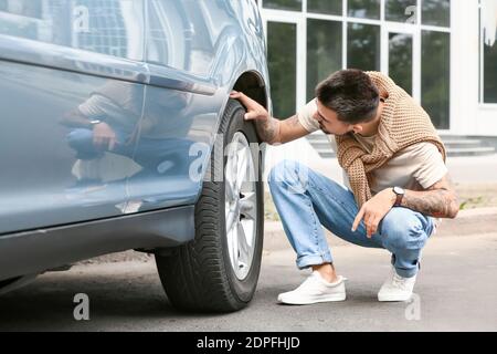 Handsome man checking tires of modern car Stock Photo