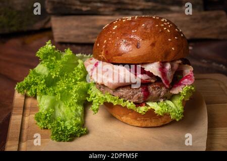 Served fresh craft beef burger with fried slices of bacon and cherry sauce, fresh lettuce laying next to it. Restaurant concept. Street food concept Stock Photo