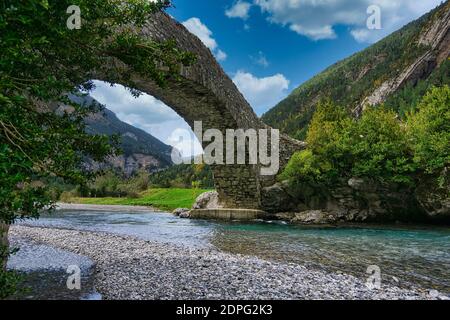 Roman bridge over river of rapid water in pyrenees Stock Photo
