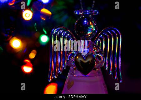 Glass angel holding a heart and supporting a halo with fairy lights on the Christmas tree behind showing as bokeh Stock Photo