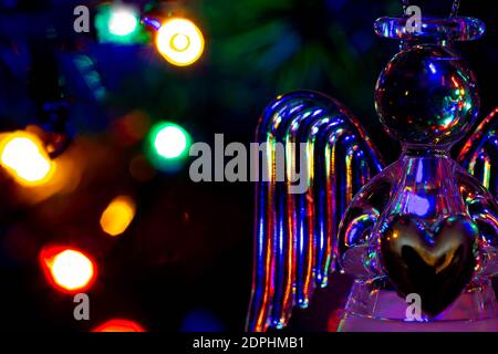 Glass angel holding a heart and supporting a halo with fairy lights on the Christmas tree behind showing as bokeh Stock Photo