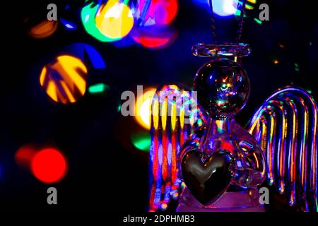 Glass angel holding a heart and supporting a halo with fairy lights on the Christmas tree behind showing as bokeh Stock Photo