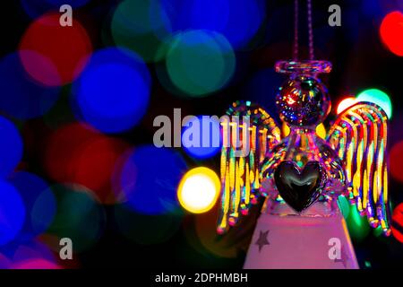 Glass angel holding a heart and supporting a halo with fairy lights on the Christmas tree behind showing as bokeh Stock Photo
