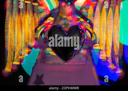 Glass angel holding a heart and supporting a halo with fairy lights on the Christmas tree behind showing as bokeh Stock Photo