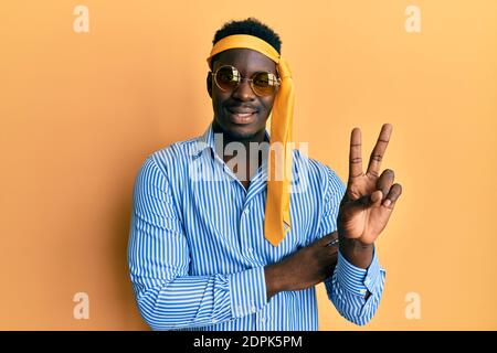 Handsome black man drunk wearing tie over head and sunglasses smiling with happy face winking at the camera doing victory sign. number two. Stock Photo