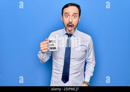 Middle age elegant business man drinking cup of coffee with best dad ever message scared and amazed with open mouth for surprise, disbelief face Stock Photo