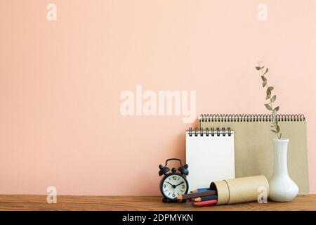 Notebook, clock, pencils with vase of eucalyptus on wooden table. pink background. Work and study place Stock Photo