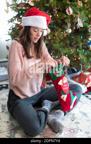 Pretty Female College Student looking at Xmas Stocking by Xmas tree Stock Photo