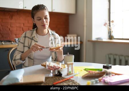 Beautiful pleased teenage girl making sandwich for breakfast before school in kitchen in morning Stock Photo