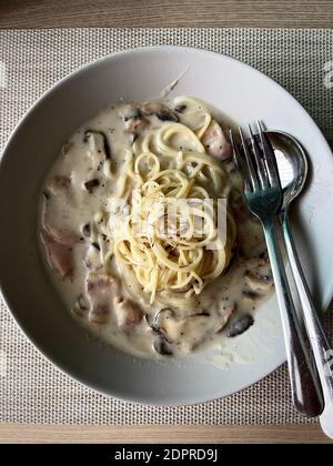 Spaghetti Cabonara pasta with white cream sauce, bacon and chicken ham on natural wooden table Stock Photo