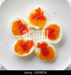 Macro close up of soft-boiled eggs, peeled and cut into two halves, and salmon caviar Stock Photo